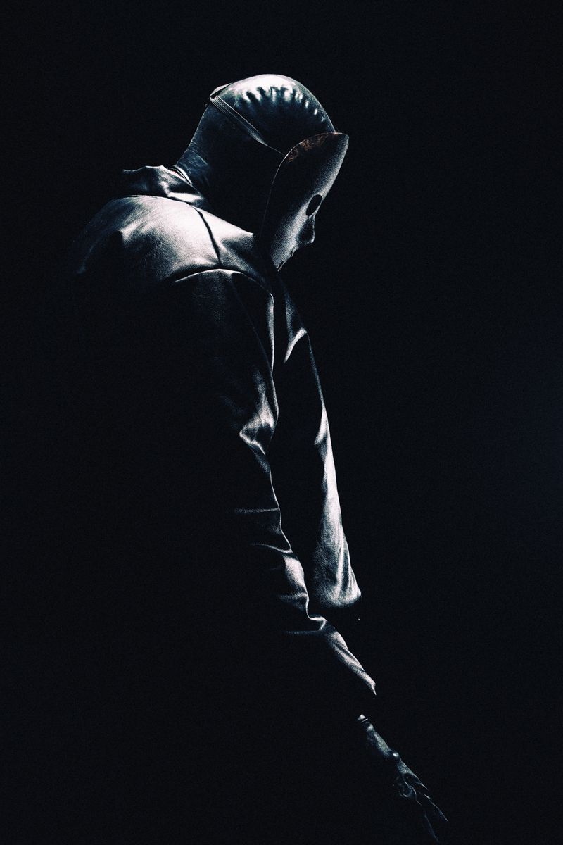 Moody silhouette of a hooded person in darkness, evoking mystery.
