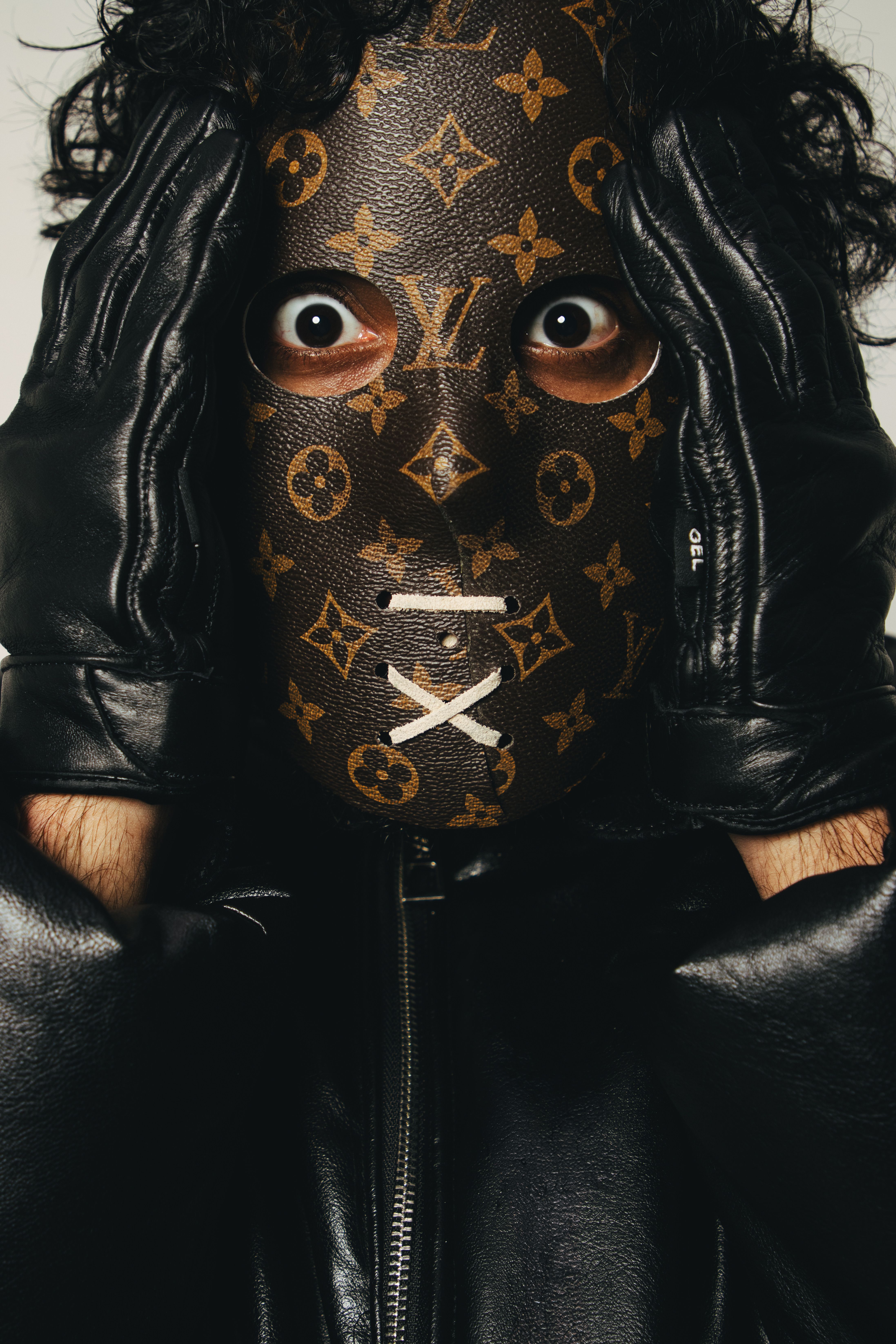 A person in a designer mask and leather gloves covers their face, creating a mysterious expression.