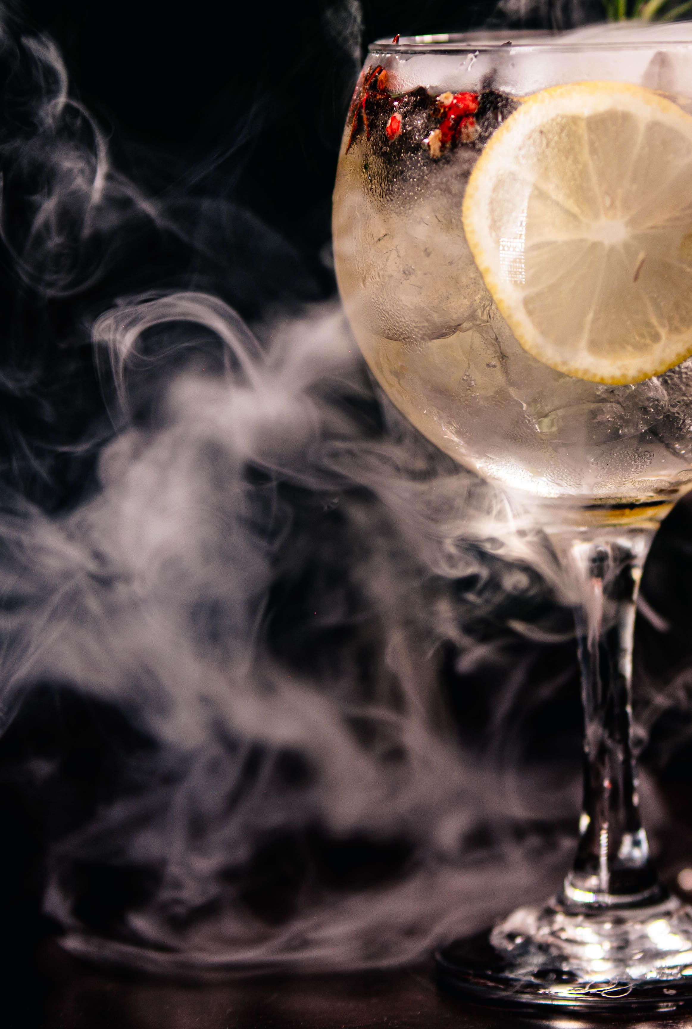 Close-up of a cocktail glass with lemon slice, berries, and mist creating a mysterious vibe.