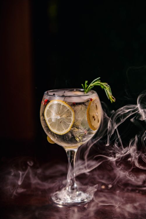 Free Elegant cocktail with lemon slices and rosemary garnish, enveloped in mysterious smoke. Stock Photo