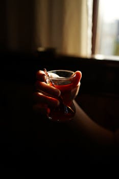 A hand gently holds a traditional Turkish tea glass in a dimly lit setting, creating a warm ambiance.