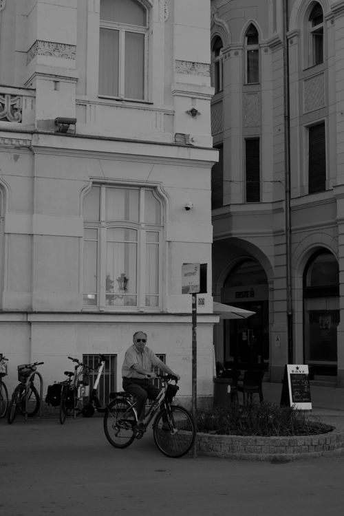 Free Black and white photo of an elderly man bicycling in a historic urban street. Stock Photo