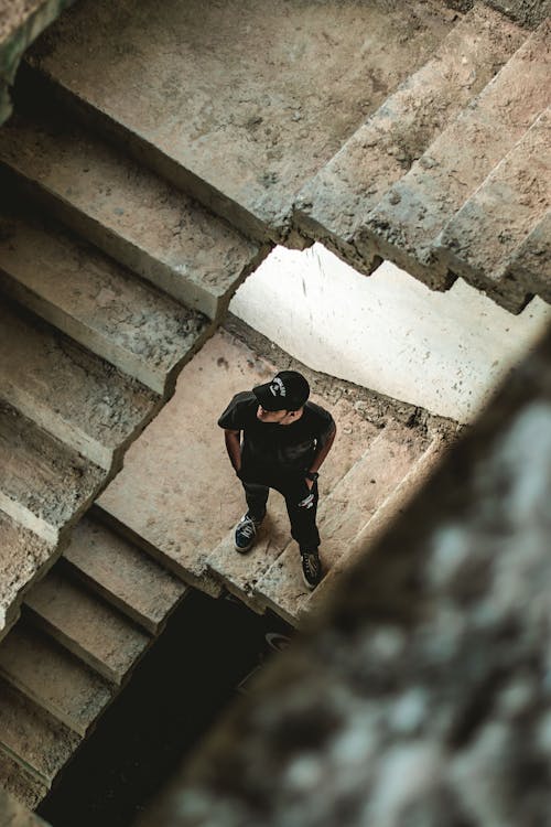 Мужчина в черной футболке с круглым вырезом стоит на бетонной лестнице