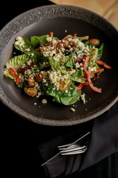 Vibrant green salad with feta, cherry tomatoes, and red peppers in a rustic bowl.