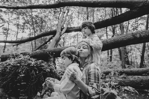Grayscale Photography of Mother and Sons Beside Tree Log