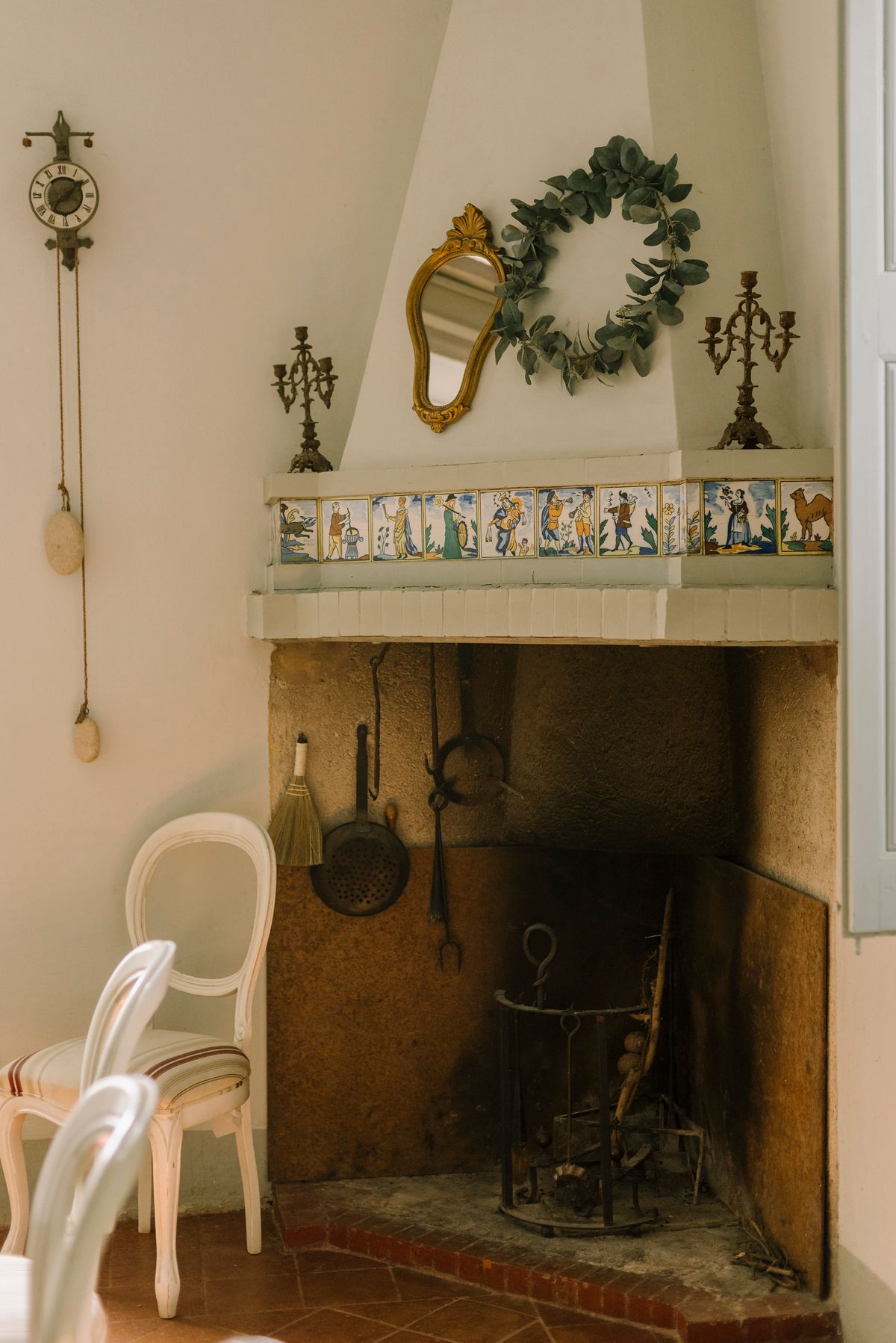 Vintage fireplace with ornate decor and wooden chair in sunlit room, exuding warmth and charm. Stock Photo.