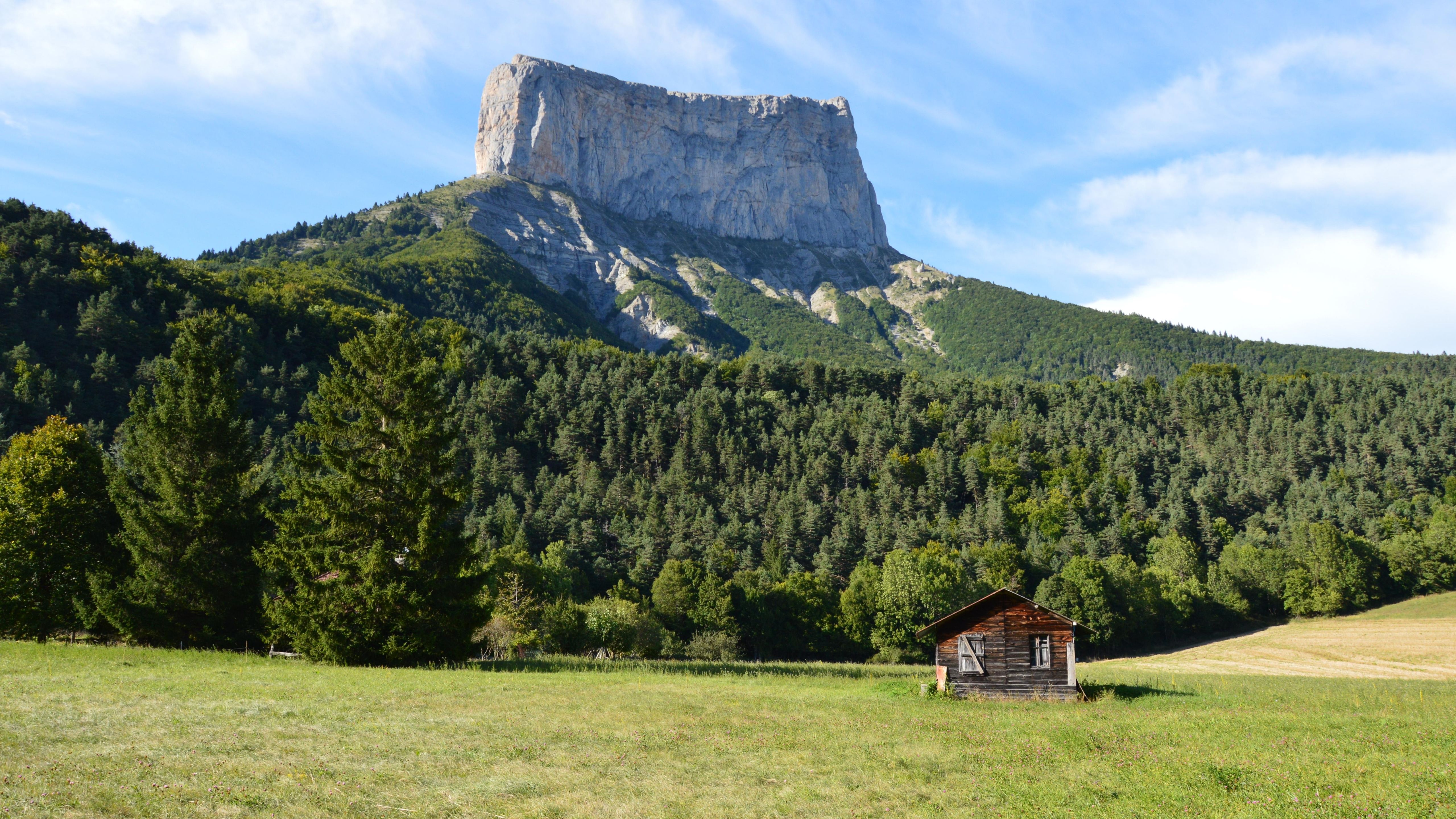 Scenic view of Mont Aiguille with a rustic cabin and lush forest in Chichilianne, France.