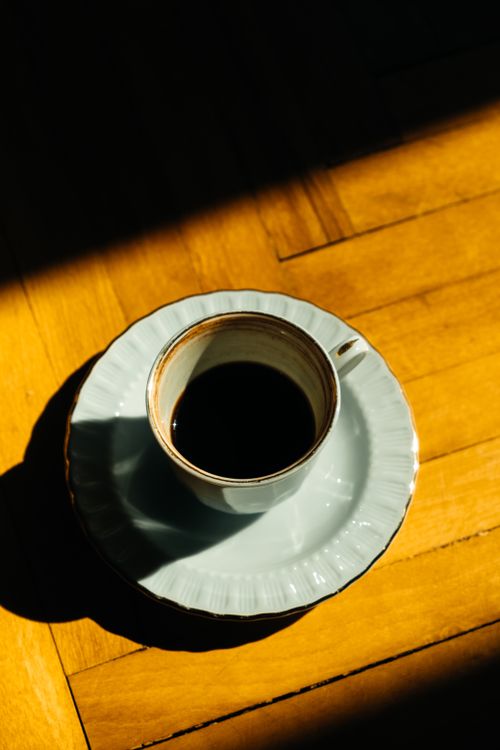 Free A ceramic coffee cup casting a shadow on a hardwood floor, captured in warm lighting. Stock Photo
