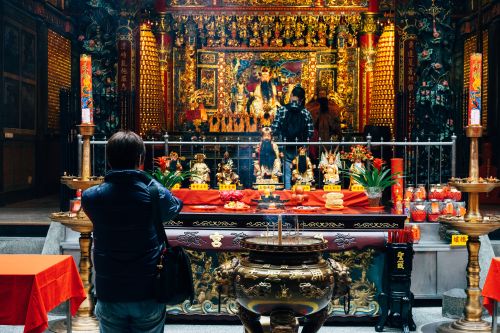 Free Intricate Chinese temple interior with visitors, showcasing ornate religious artifacts and vibrant decorations. Stock Photo