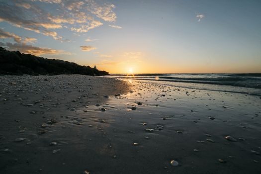 A tranquil beach scene at sunset with gentle waves and a reflective shoreline, capturing the natural beauty of the ocean.