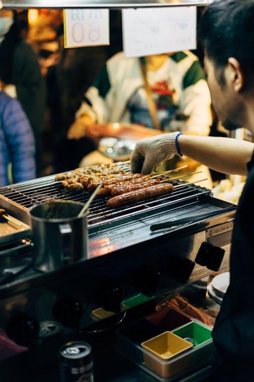 Selective Focus Photo of a Man Grilling  Skewered Sausages