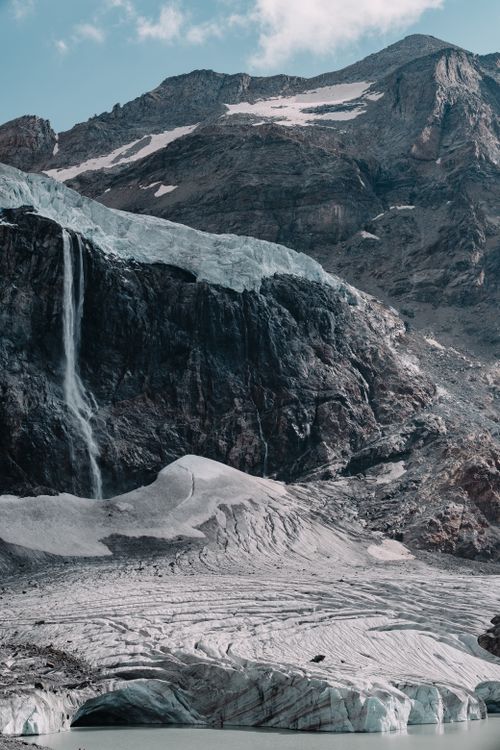 Free Stunning view of a glacier and waterfall against rugged mountain terrain. Stock Photo
