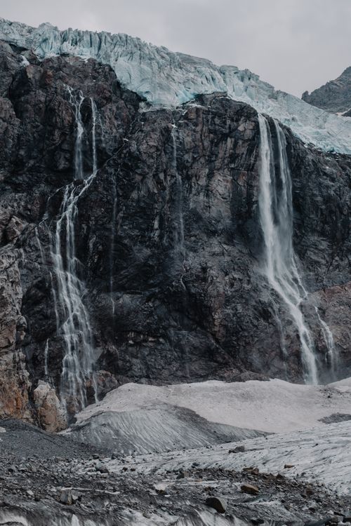 Free Glacial waterfalls cascading over rocky cliffs create a striking natural landscape. Stock Photo