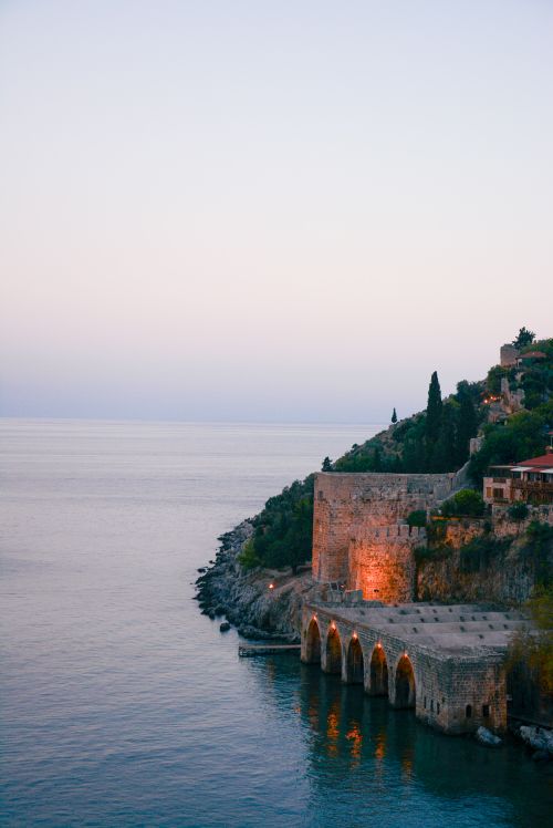 Free A tranquil coastal scene with an ancient fortress glowing at sunset by the sea. Stock Photo