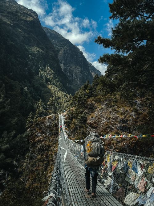 Free A hiker crosses a suspension bridge surrounded by stunning Himalayan views in Namche, Nepal. Stock Photo
