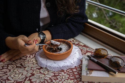A warm moment enjoying chocolate dessert near a window with a view, featuring styled accessories.