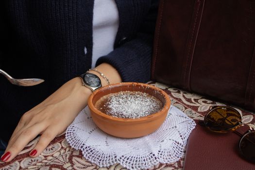 Clay bowl with powdered dessert and hand resting on patterned table in Istanbul, Türkiye.