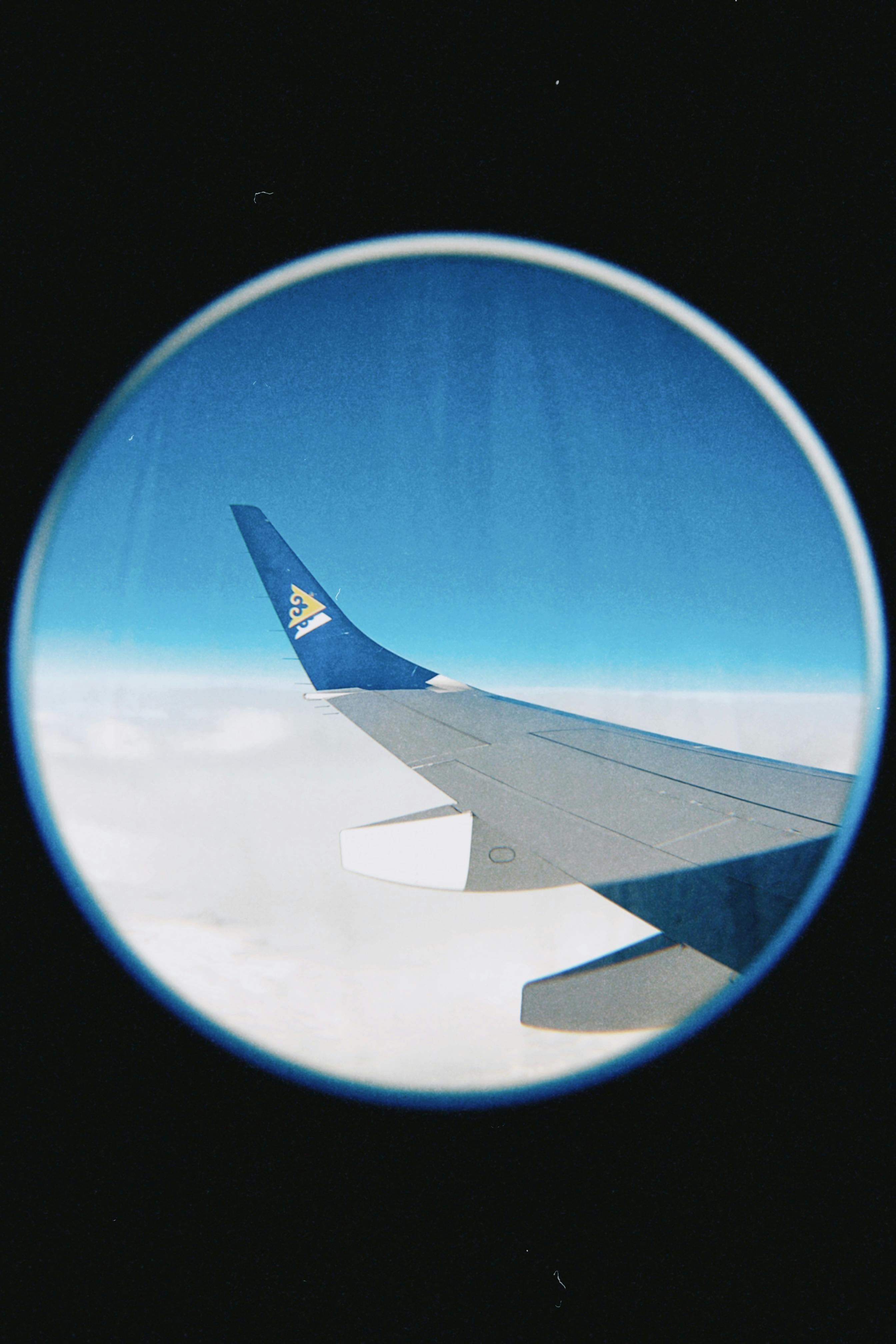 View of an airplane wing above the clouds captured through a fish eye lens, showcasing a clear blue sky.