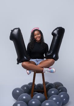 Happy teenage girl celebrating eleventh birthday with balloons and tiara.