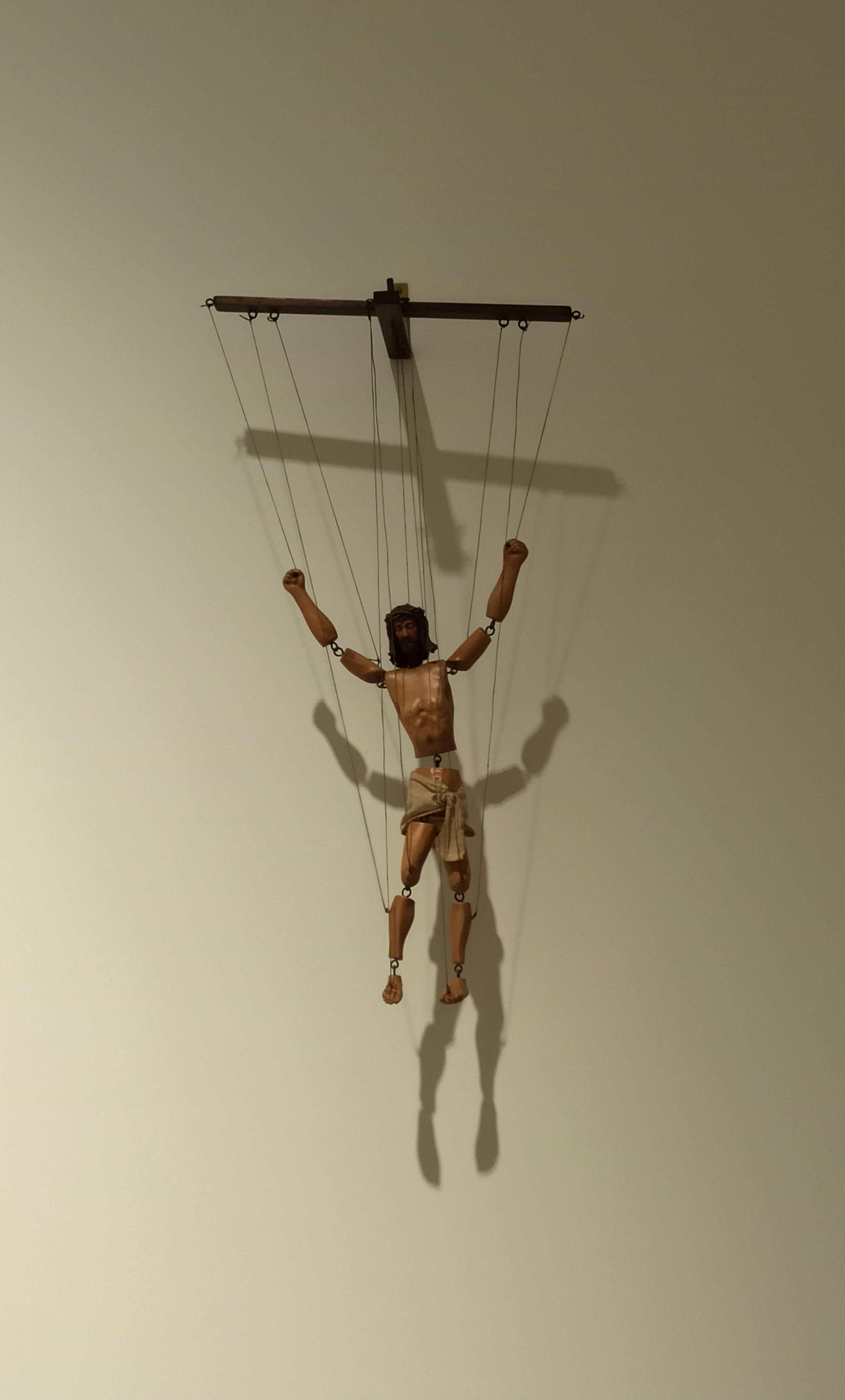 Free A wooden marionette puppet hangs suspended against a neutral background. Stock Photo