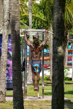 Fit man exercising with pull-ups on outdoor equipment in a park setting for strength training.