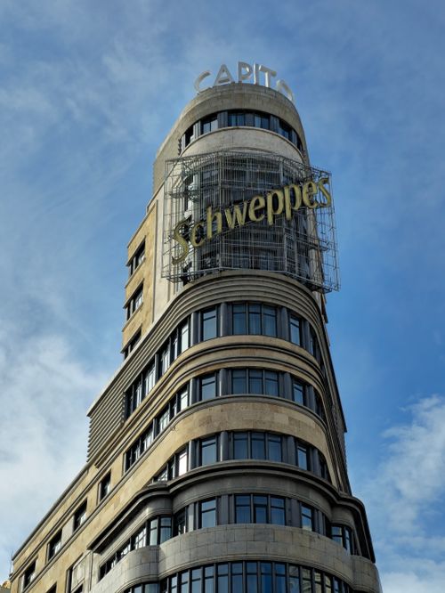 Free View of the Capitol Building in Madrid featuring the iconic Schweppes sign against a blue sky. Stock Photo