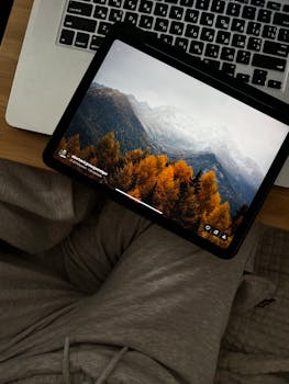A cozy home office setup with a laptop and tablet displaying a mountain landscape.