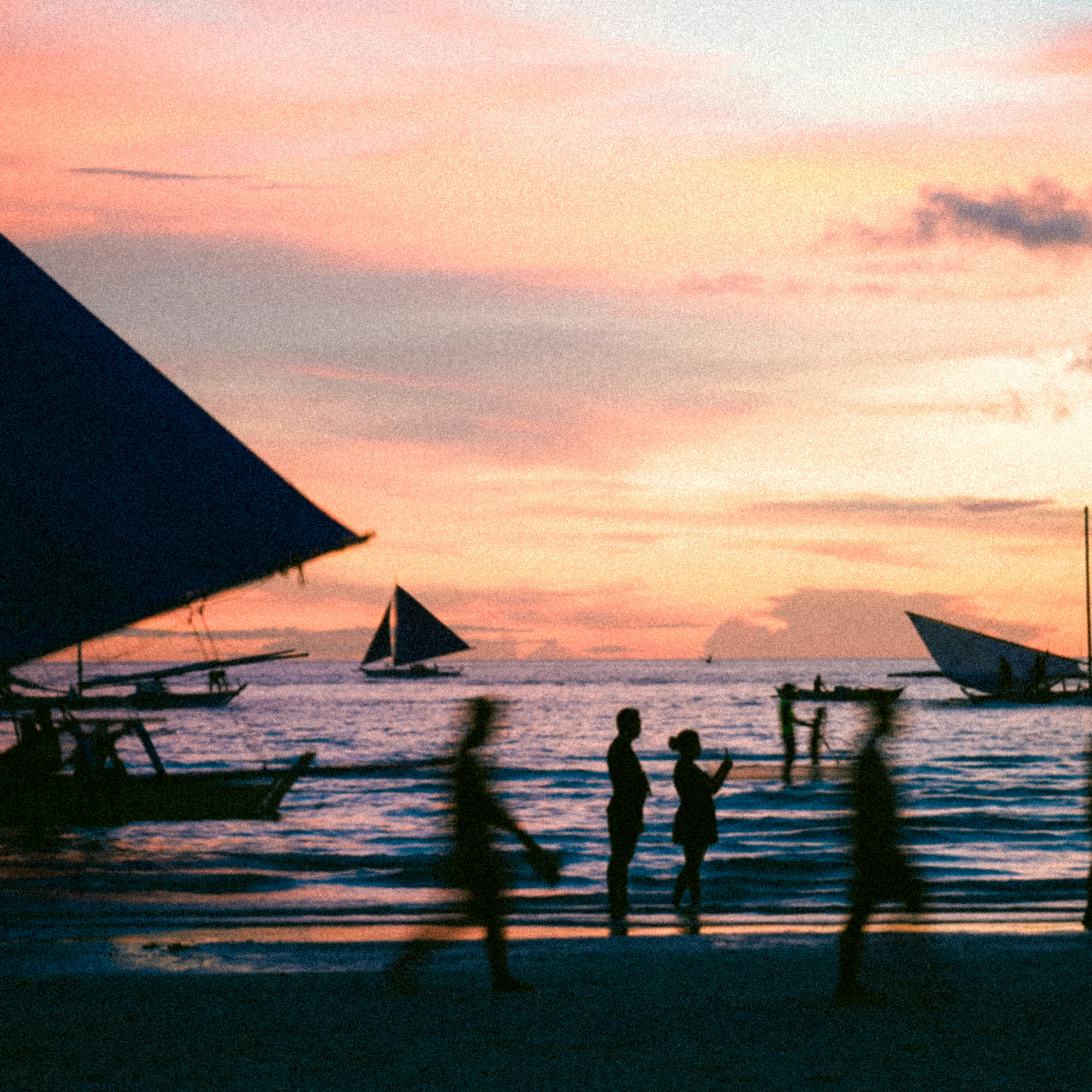 Silhouettes on a beach with vibrant sky and boats during a stunning sunset.