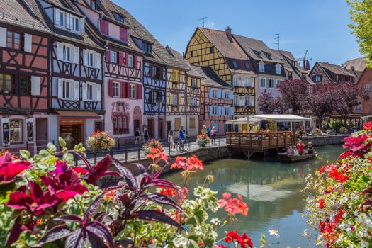 Colorful medieval houses along a canal in Colmar, France, with vibrant flowers and sunny skies.