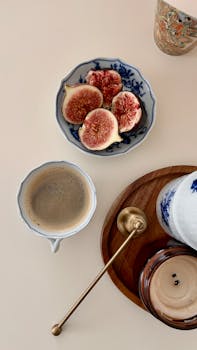 A stylish breakfast setting featuring figs on a porcelain dish, a cup of coffee, and decorative tableware.