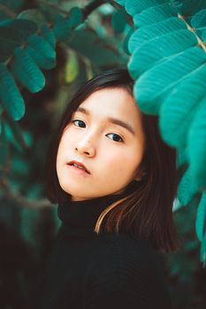 一幅描绘迷人亚洲女性的肖像画，被充满活力的绿叶环绕，展现出美丽与宁静