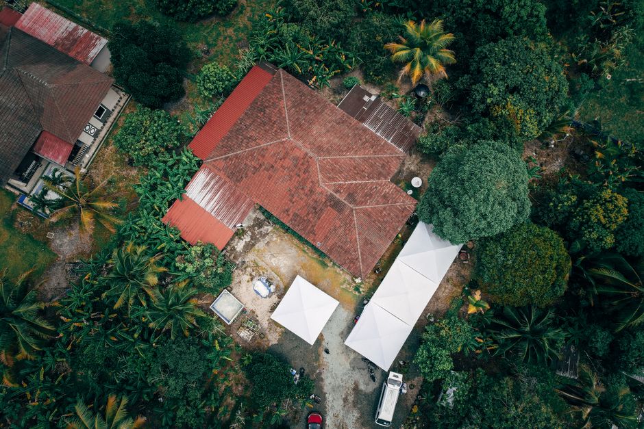 Aerial shot of a rural house with a red roof surrounded by lush tropical greenery.