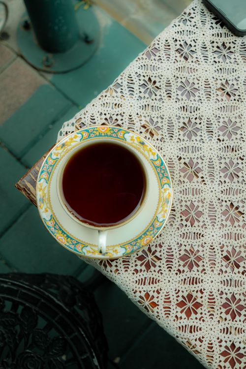 Free A delicate teacup filled with tea on a lace-covered table outdoors. Elegant and serene. Stock Photo