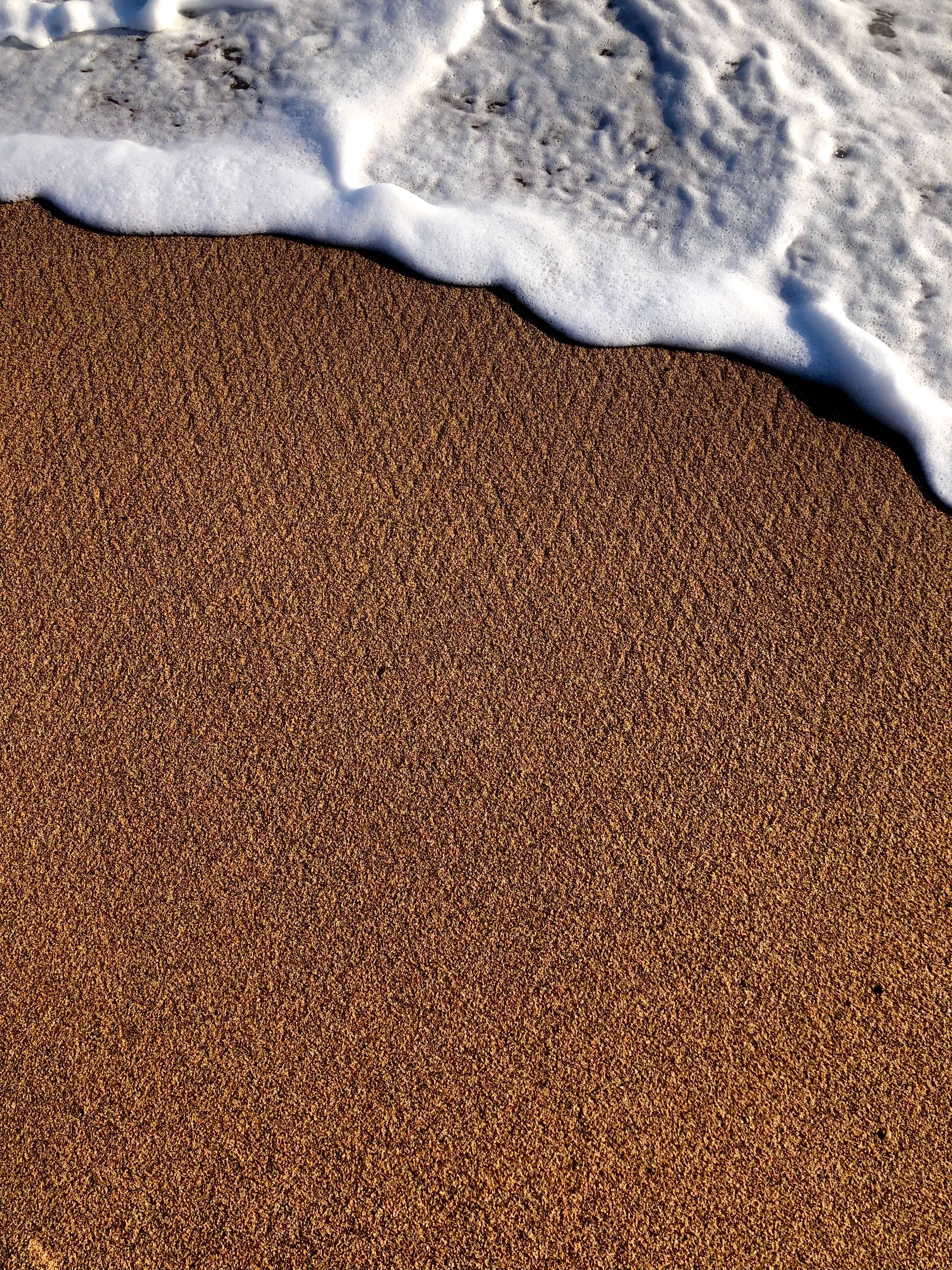 Close-up of a gentle ocean wave reaching the sandy beach with textured shoreline.