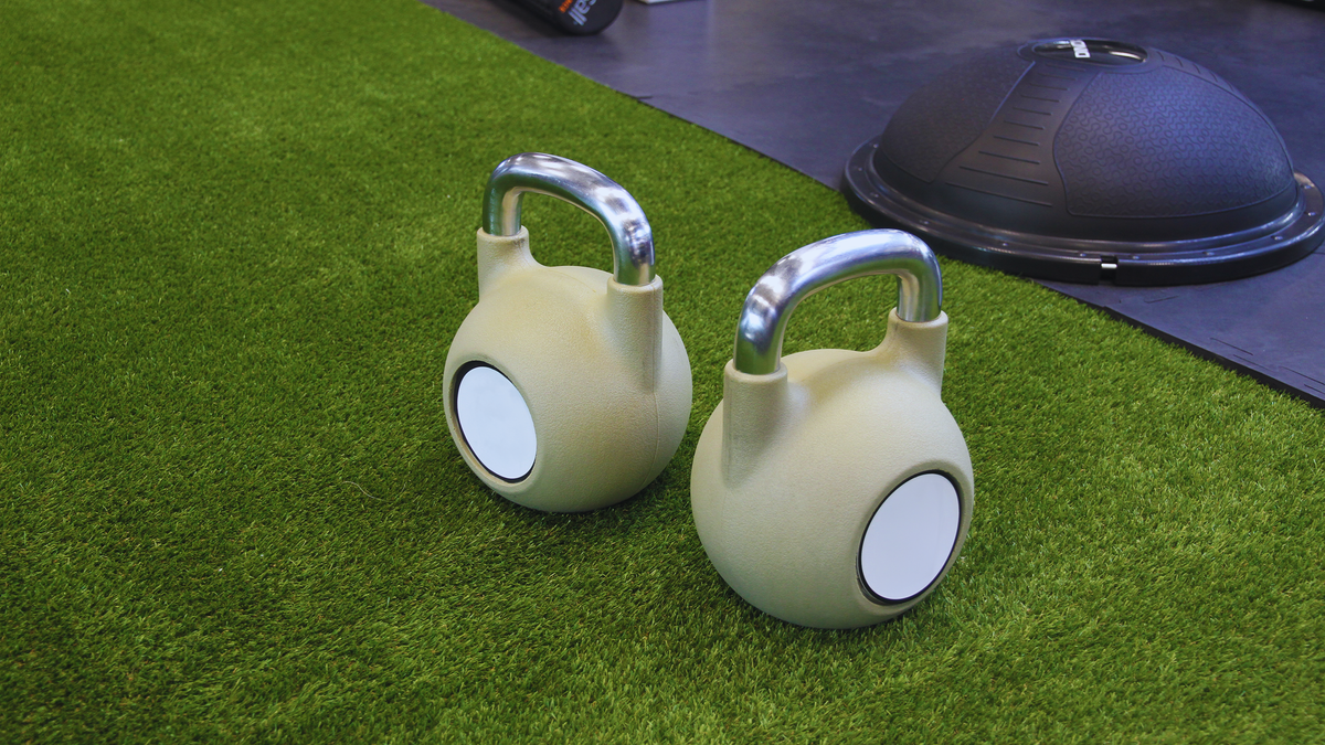 Two kettlebells on a green artificial grass floor in an indoor gym, ideal for strength training.