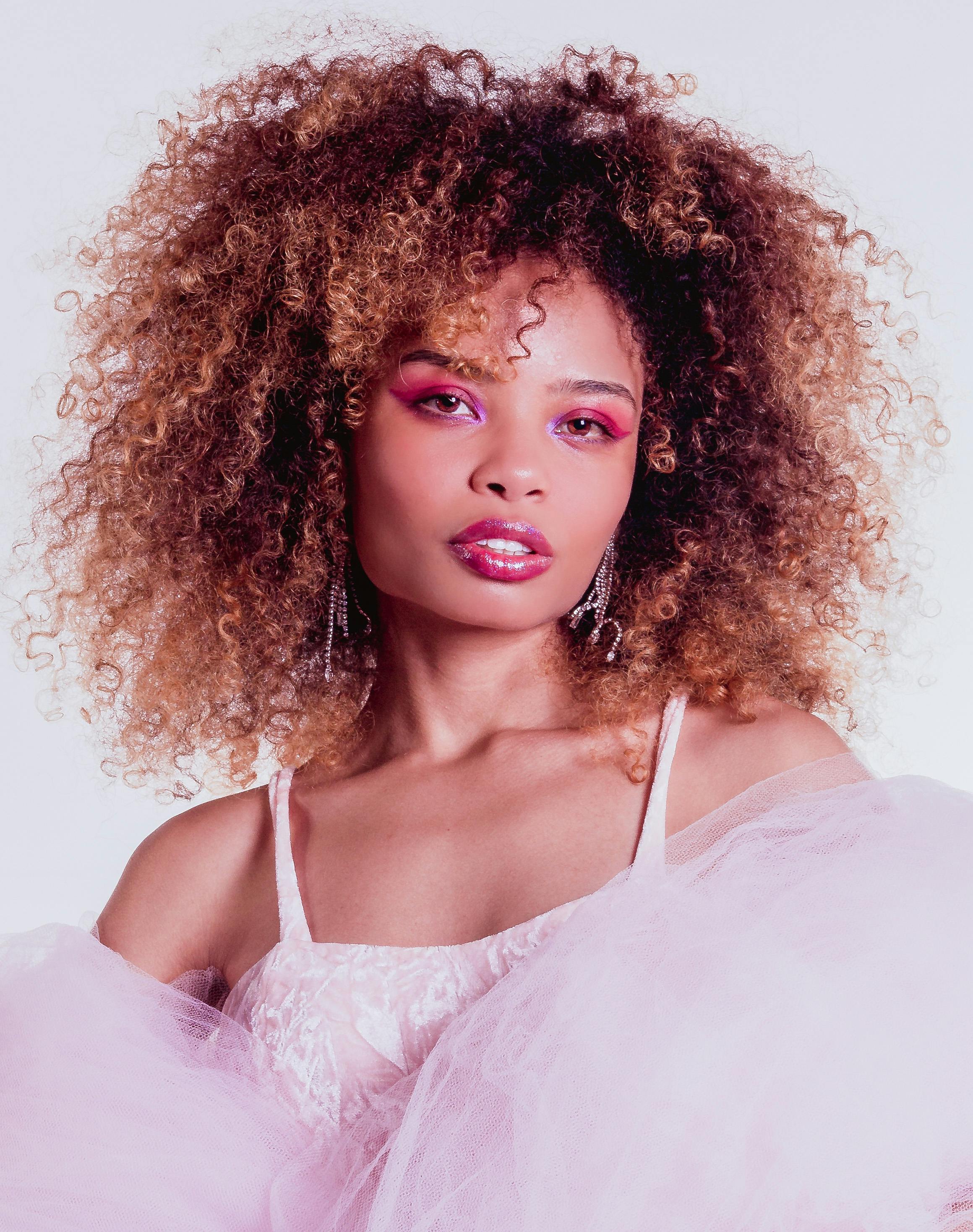 Stylish portrait of a woman with curly hair and pink attire, exuding elegance and grace.