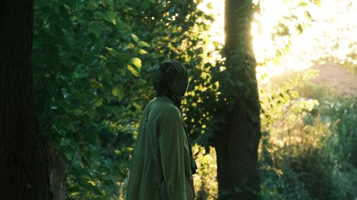 Free A woman in a green dress stands in a lush forest with sunlight filtering through. Stock Photo