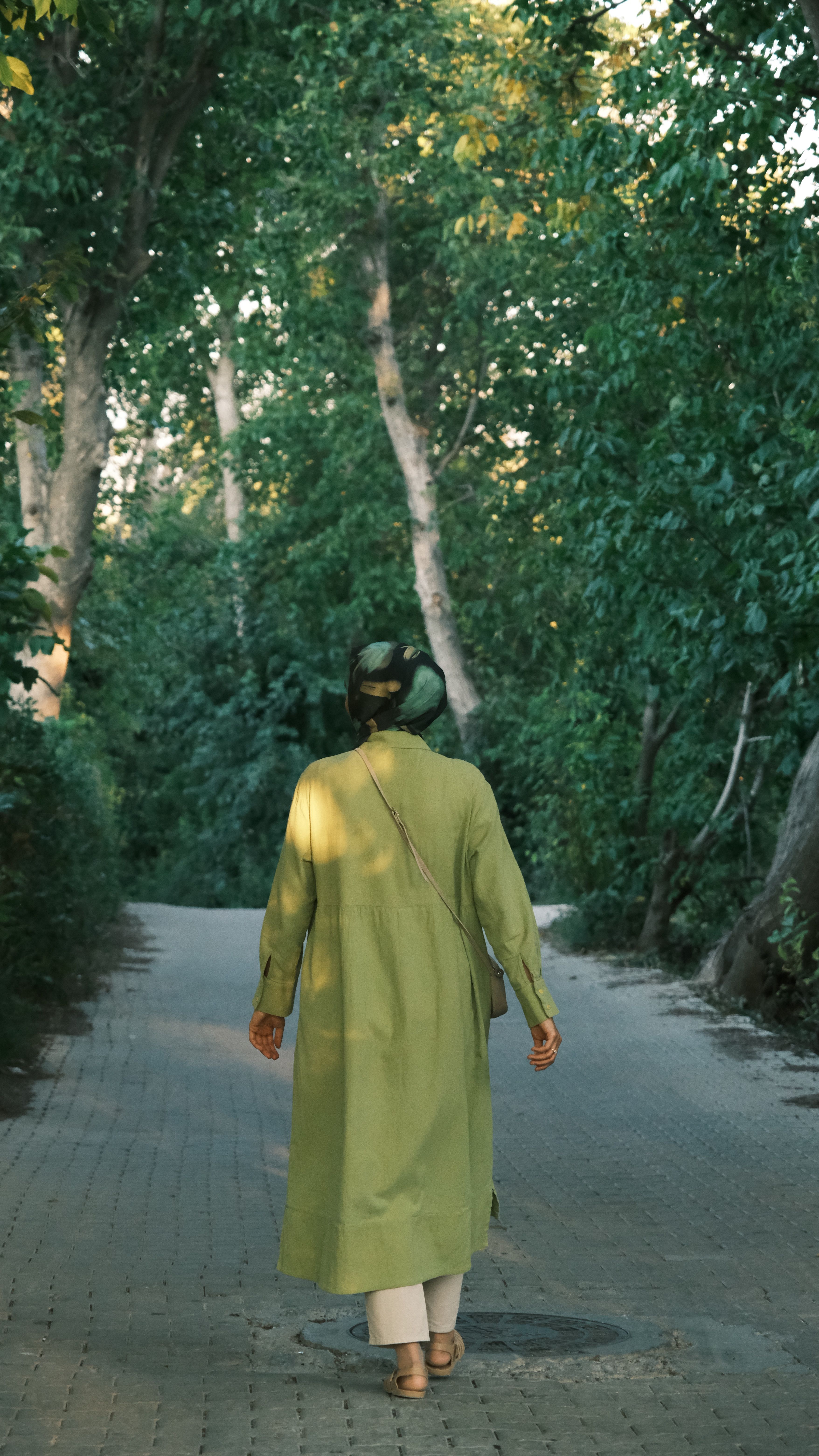 Serene scene of a woman walking in a green coat on a forest path.