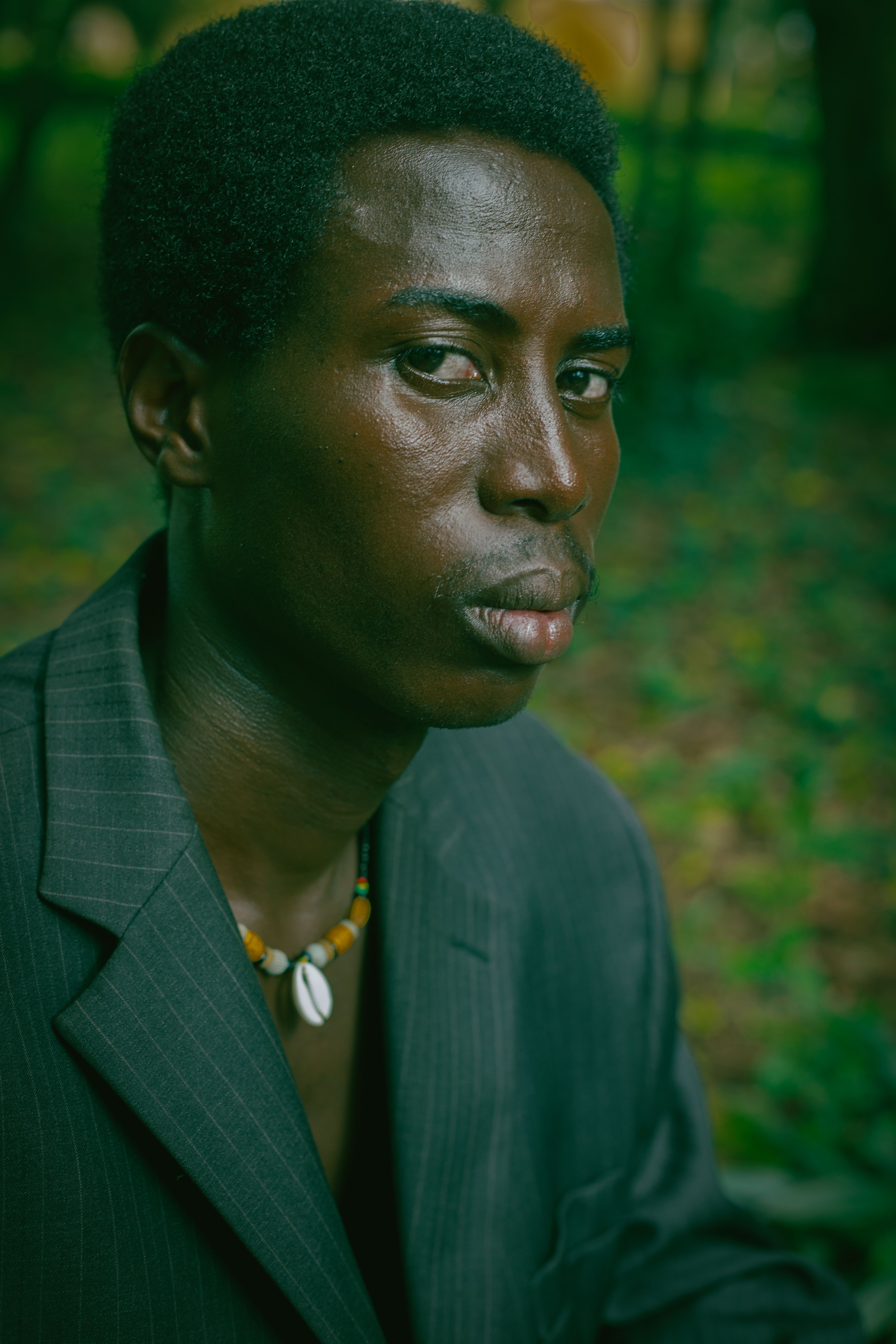 Close-up portrait of an adult man wearing a beaded necklace, set against an outdoor background in Accra, Ghana.