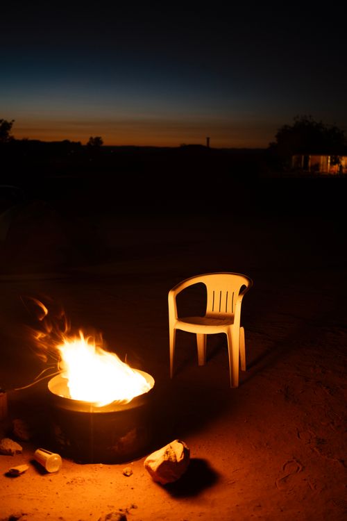 Free A tranquil campfire scene at twilight with an empty plastic chair under a starlit sky. Stock Photo