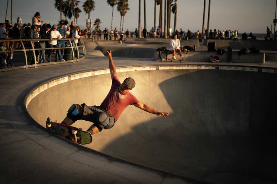 Action shot of a skateboarder performing at Venice Beach skatepark during sunset, surrounded by spectators.