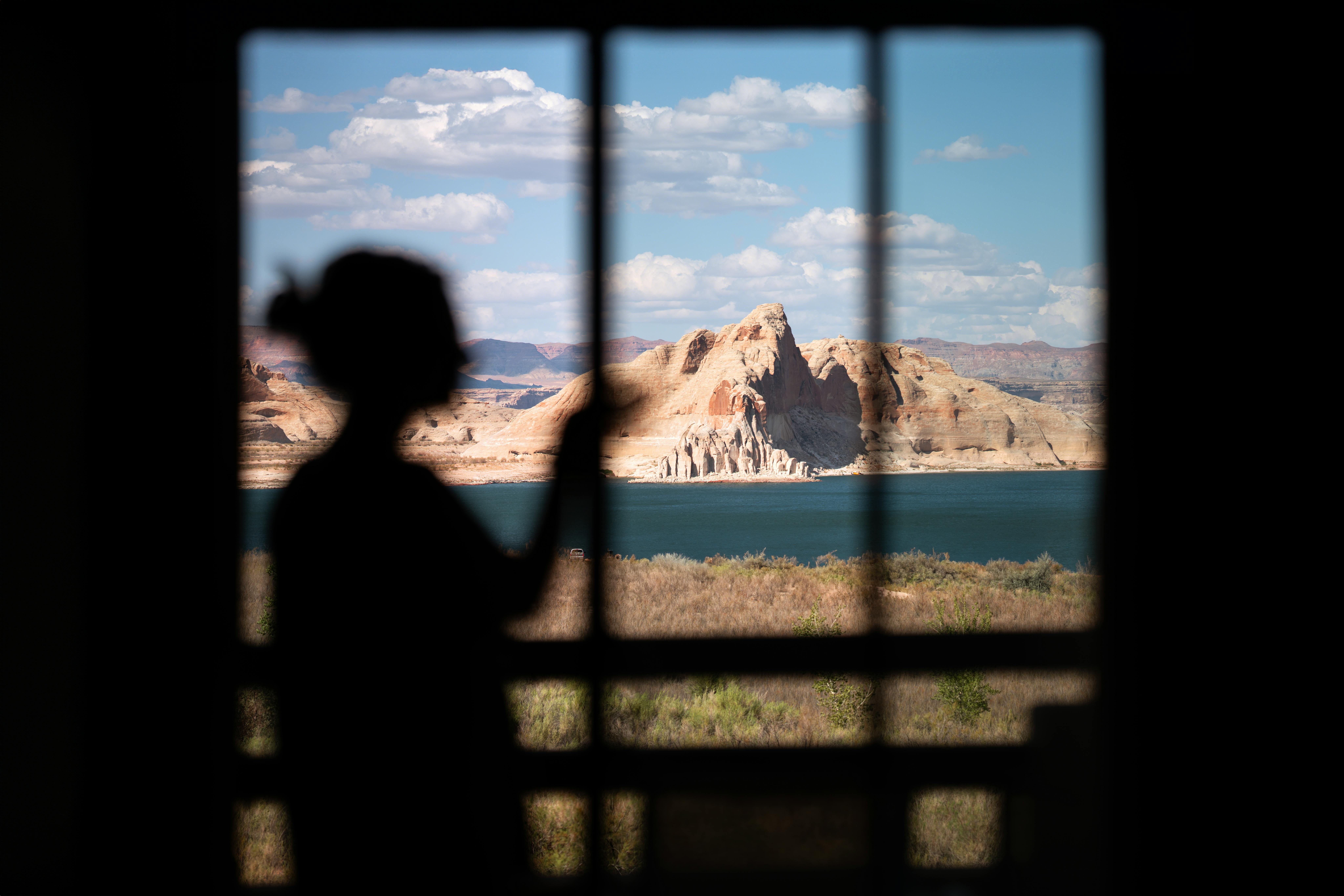 Silhouette of a woman gazing at Lake Powell through a window, with desert landscape.