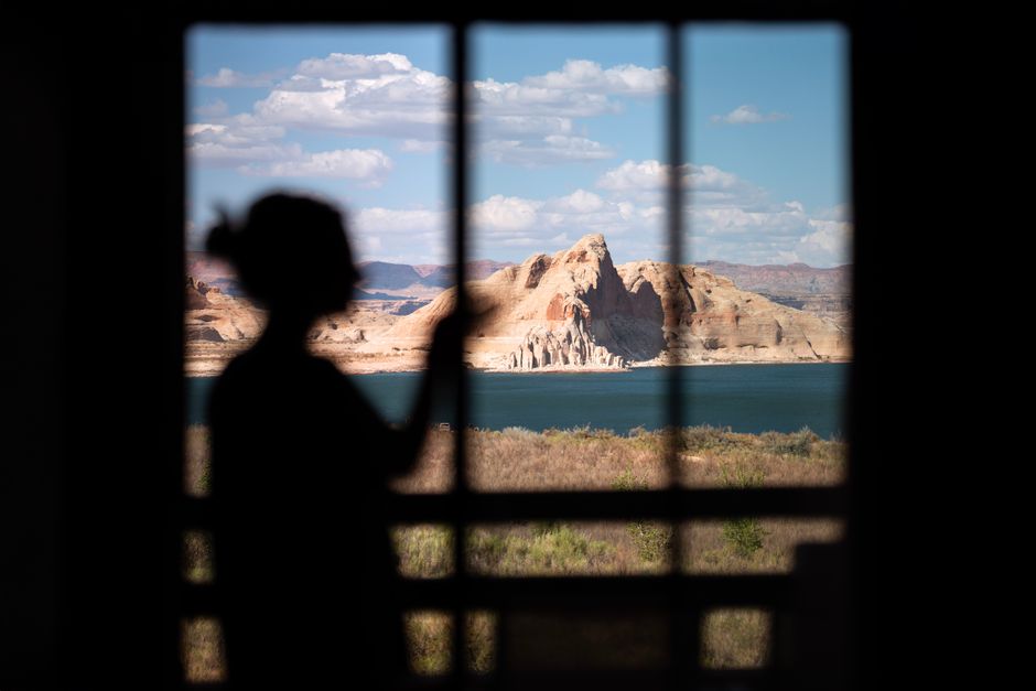 Silhouette of a woman gazing at Lake Powell through a window, with desert landscape.