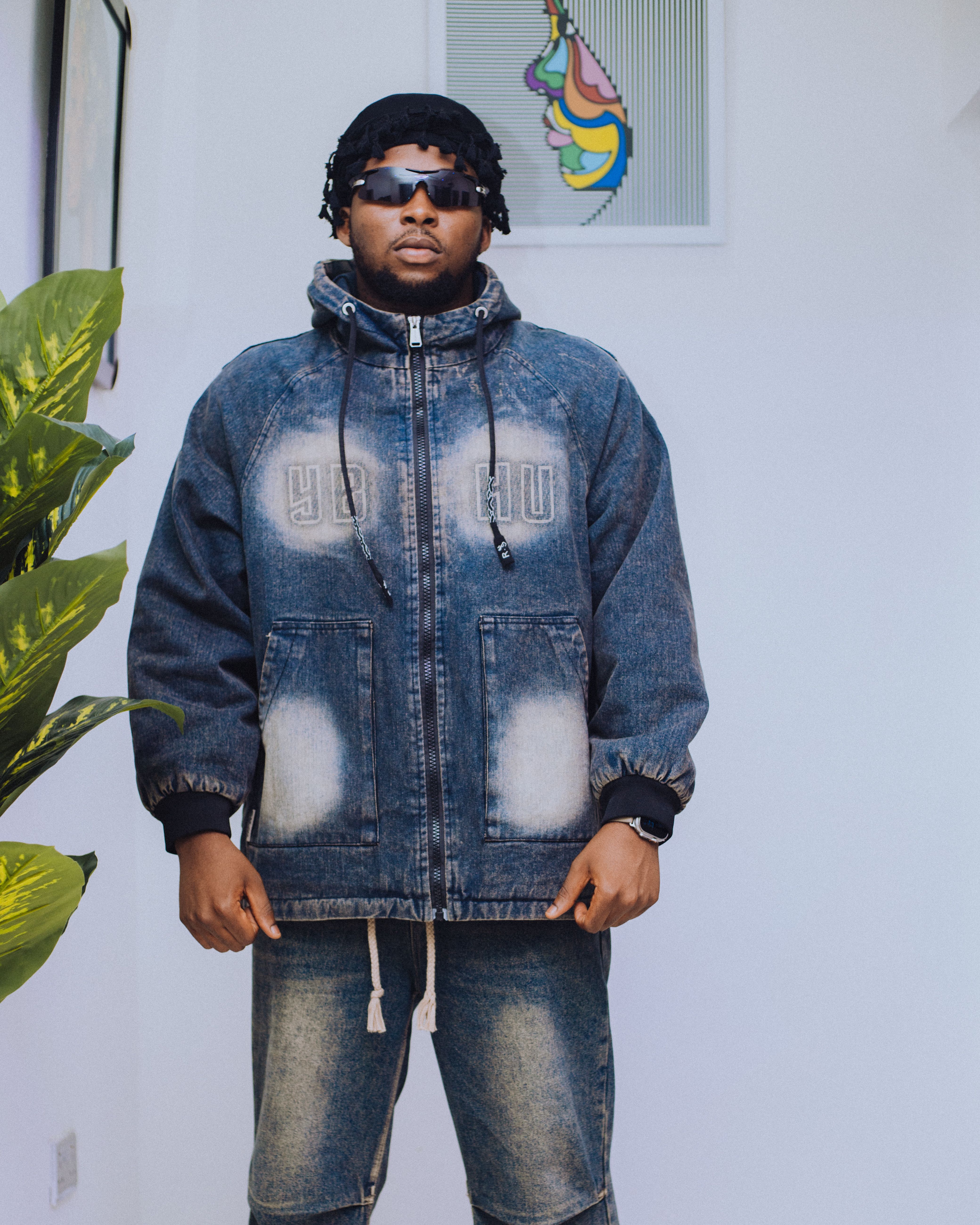 Fashionable man wearing a trendy denim jacket and sunglasses indoors.