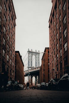 Iconic view of Manhattan Bridge framed by buildings in Brooklyn, NY. Urban architecture with a dramatic vibe.