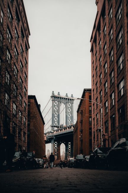 Iconic view of Manhattan Bridge framed by buildings in Brooklyn, NY. Urban architecture with a dramatic vibe.