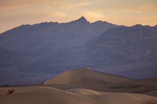Scenic view of sand dunes against rugged mountains at sunset in Death Valley National Park.