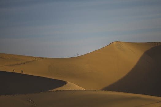 Dramatic landscape of sandy desert dunes with tourists exploring under a clear day sky.