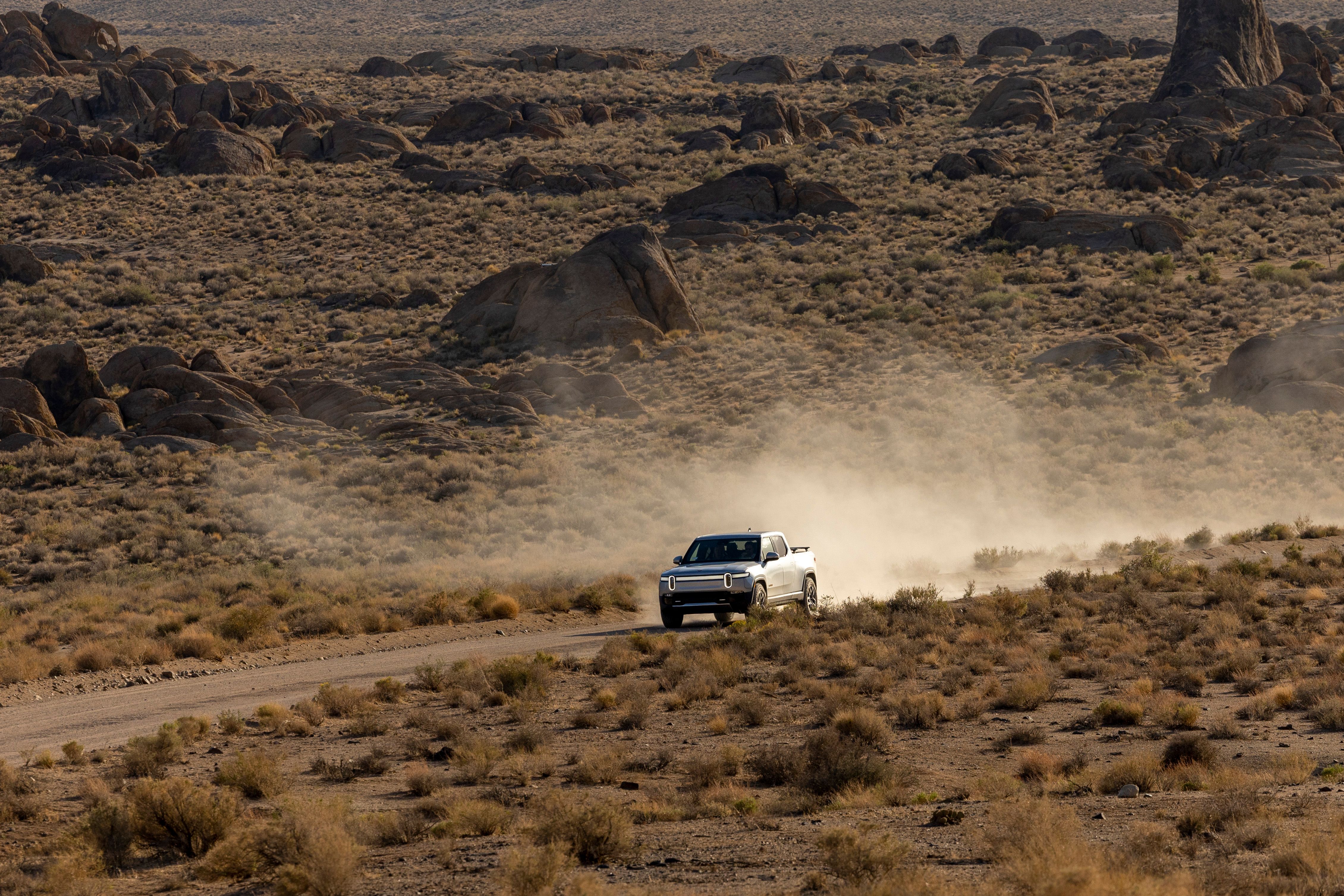 White SUV driving on a dusty road in a rocky desert, creating dramatic dust clouds.