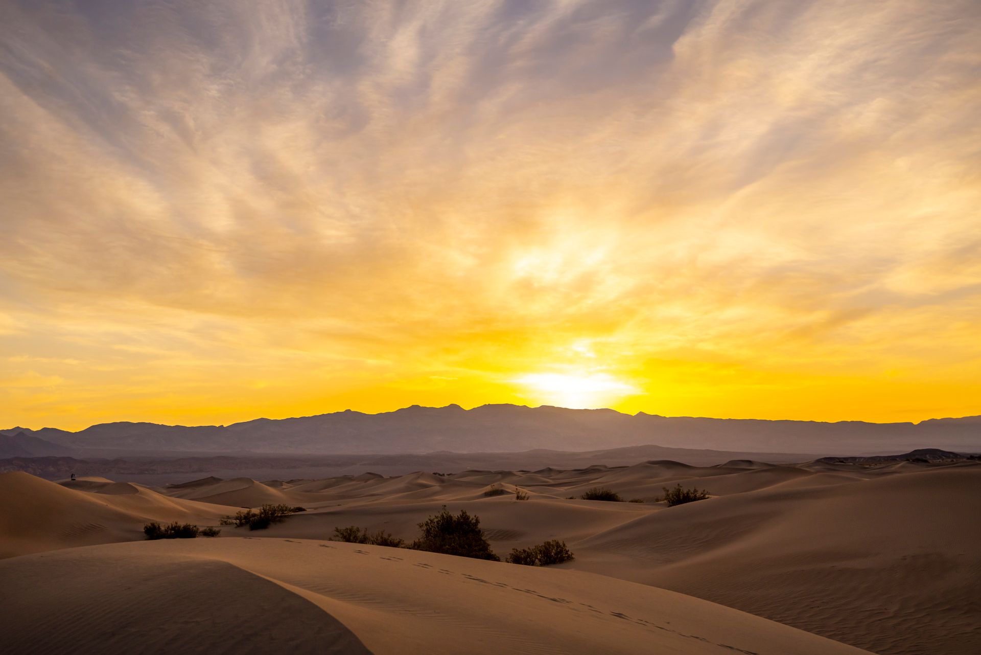 Golden sunset over Mesquite Flat Sand Dunes with dramatic sky and mountains in Death Valley.